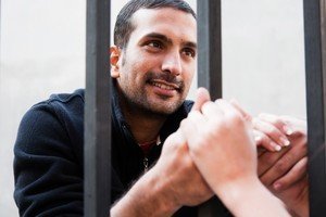 Inmate behind bars, holding hands through the bars and smiling